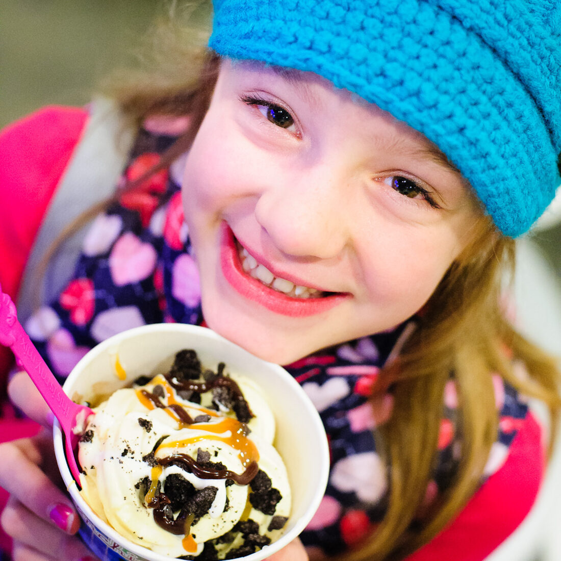 A smiling girl holding a cup of frozen yogurt with toppings
